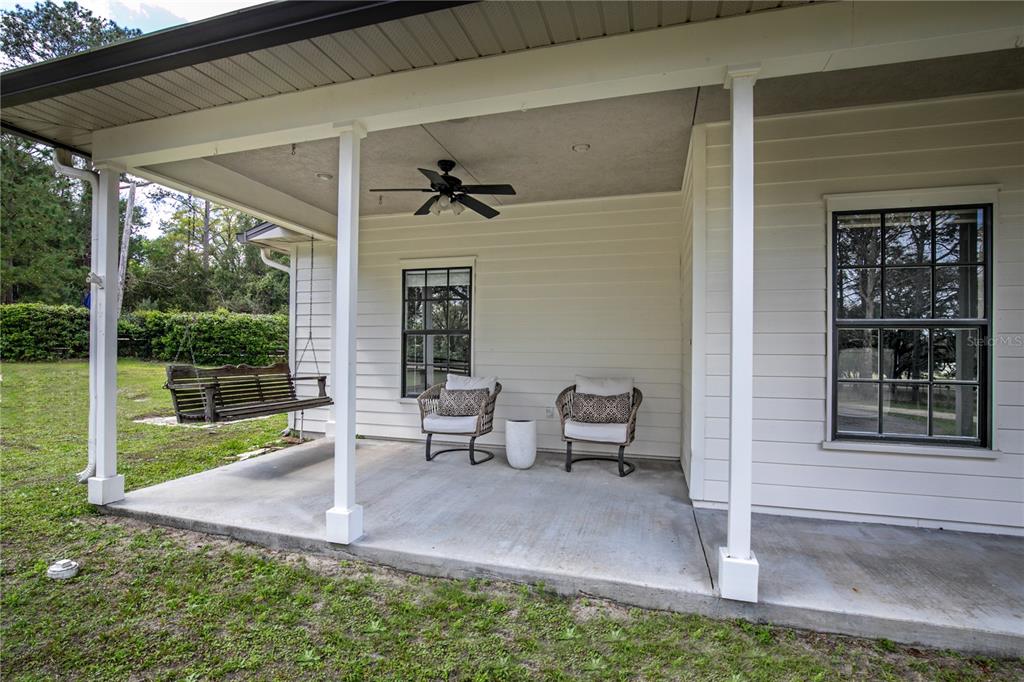 A covered concrete patio features a porch swing, two chairs, and a ceiling fan — 22301 CORONADO SOMERSET DRIVE, SORRENTO, FL