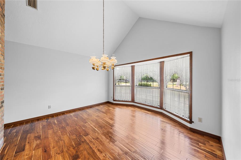 An empty dining room with hardwood floors, a vaulted ceiling, and a large bay window — 10500 SW 65TH TERRACE, OCALA, FL
