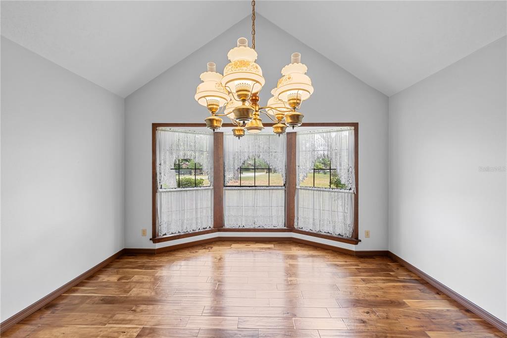 A dining room with hardwood floors, a vaulted ceiling, and a bay window with curtains — 10500 SW 65TH TERRACE, OCALA, FL