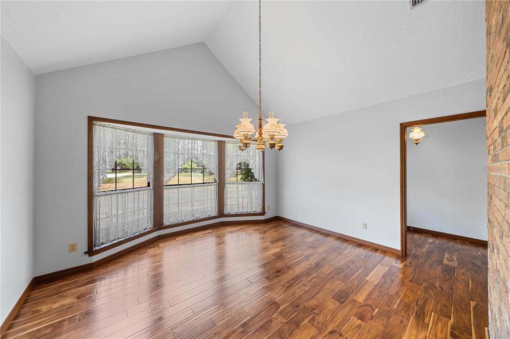 A dining room with vaulted ceilings, hardwood floors, a bay window, and a chandelier — 10500 SW 65TH TERRACE, OCALA, FL