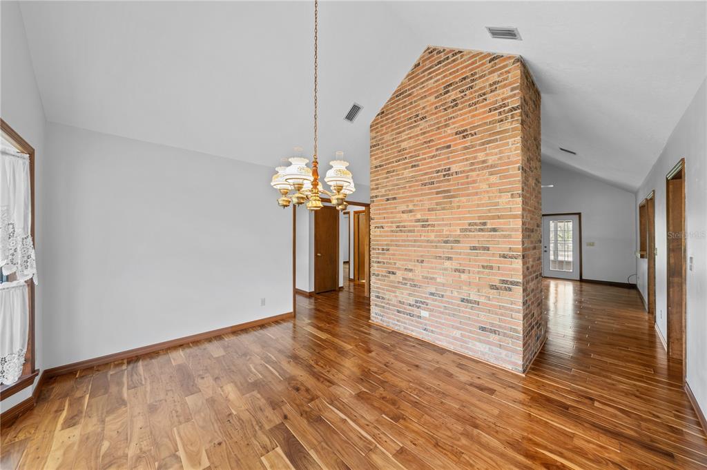 A dining room features a tall brick fireplace, vaulted ceilings, and hardwood flooring — 10500 SW 65TH TERRACE, OCALA, FL