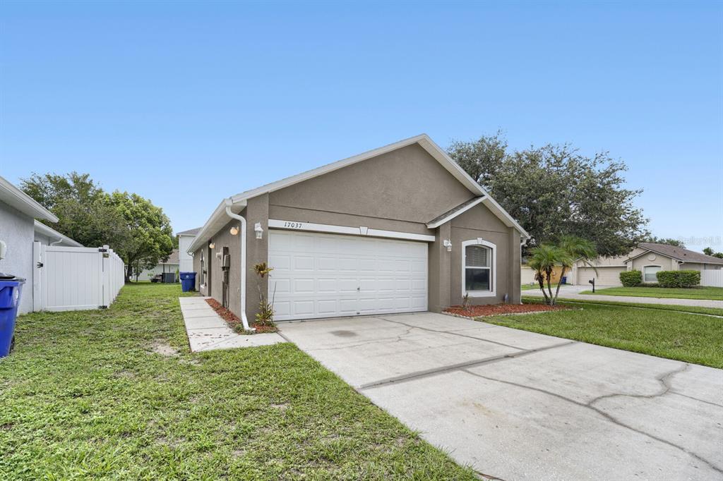 A single-story house with a beige stucco exterior, a two-car garage, and a concrete driveway — 17037 HOLMBY COURT, LAND O LAKES, FL