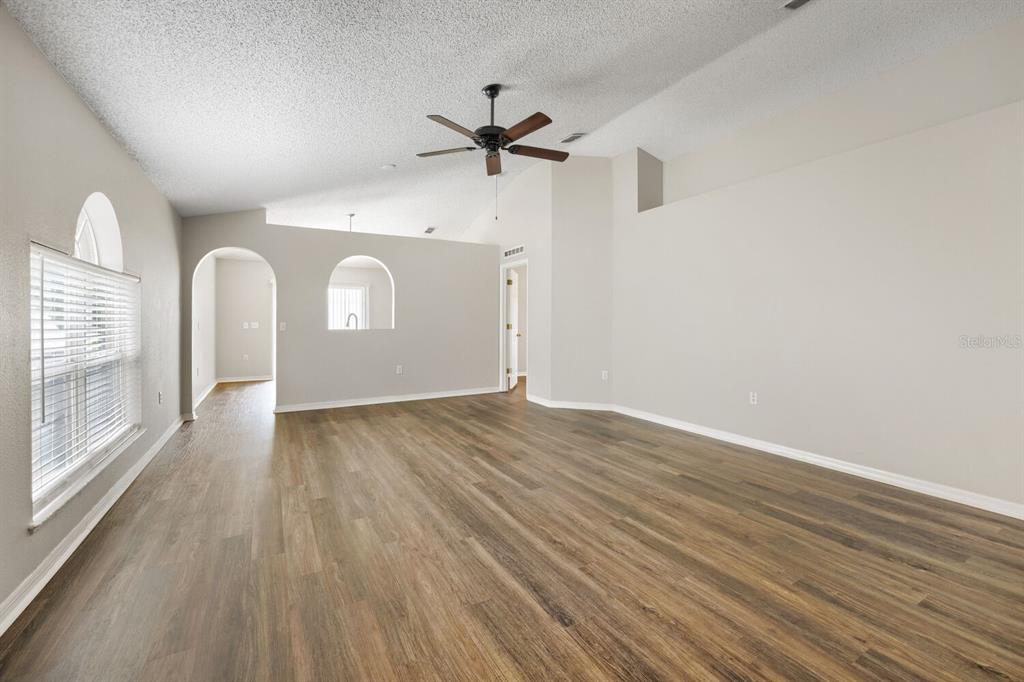 An empty living room features vaulted ceilings, a ceiling fan, and wood-look laminate flooring — 17037 HOLMBY COURT, LAND O LAKES, FL