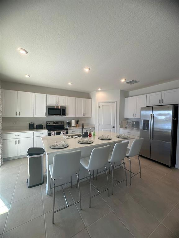 A kitchen features white cabinetry, stainless steel appliances, and a central island with bar seating — 3921 SOUTHERN VISTA LOOP, ST CLOUD, FL