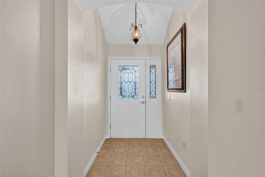 An entryway features a white front door with a glass insert, tiled flooring, and vaulted ceilings — 1557 OAK FOREST DRIVE, THE VILLAGES, FL