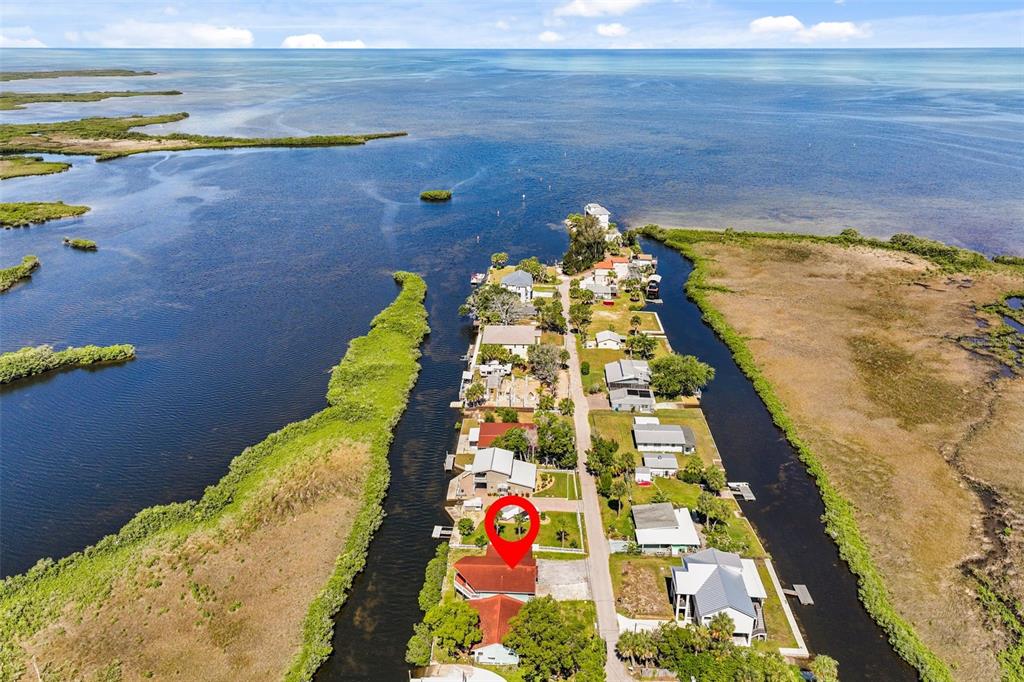 An aerial view shows a waterfront house with a red roof on a narrow peninsula — 3016 SUNSET VISTA DRIVE, SPRING HILL, FL