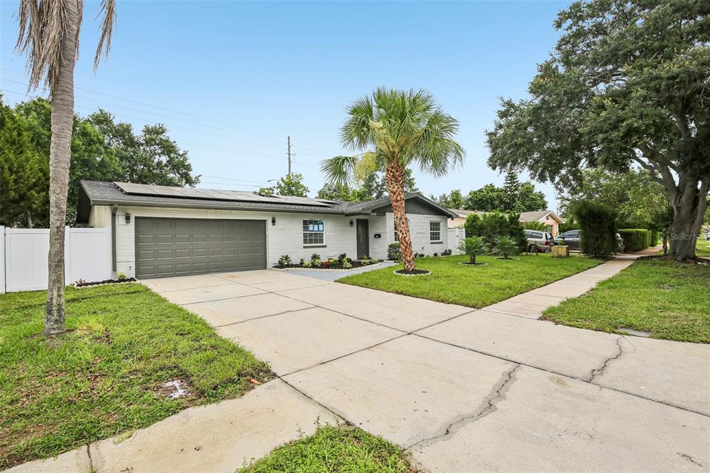 A single-story white brick house with a gray garage door and solar panels on roof — 2230 ALBRIGHT DRIVE, CLEARWATER, FL