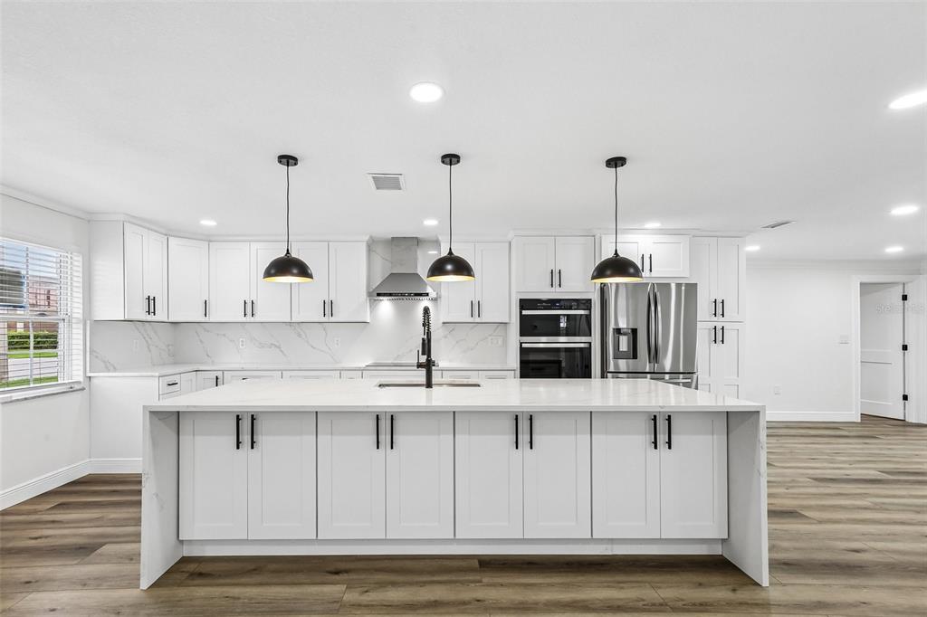 A modern white kitchen features a large island, stainless steel appliances, and wood-look flooring — 2230 ALBRIGHT DRIVE, CLEARWATER, FL