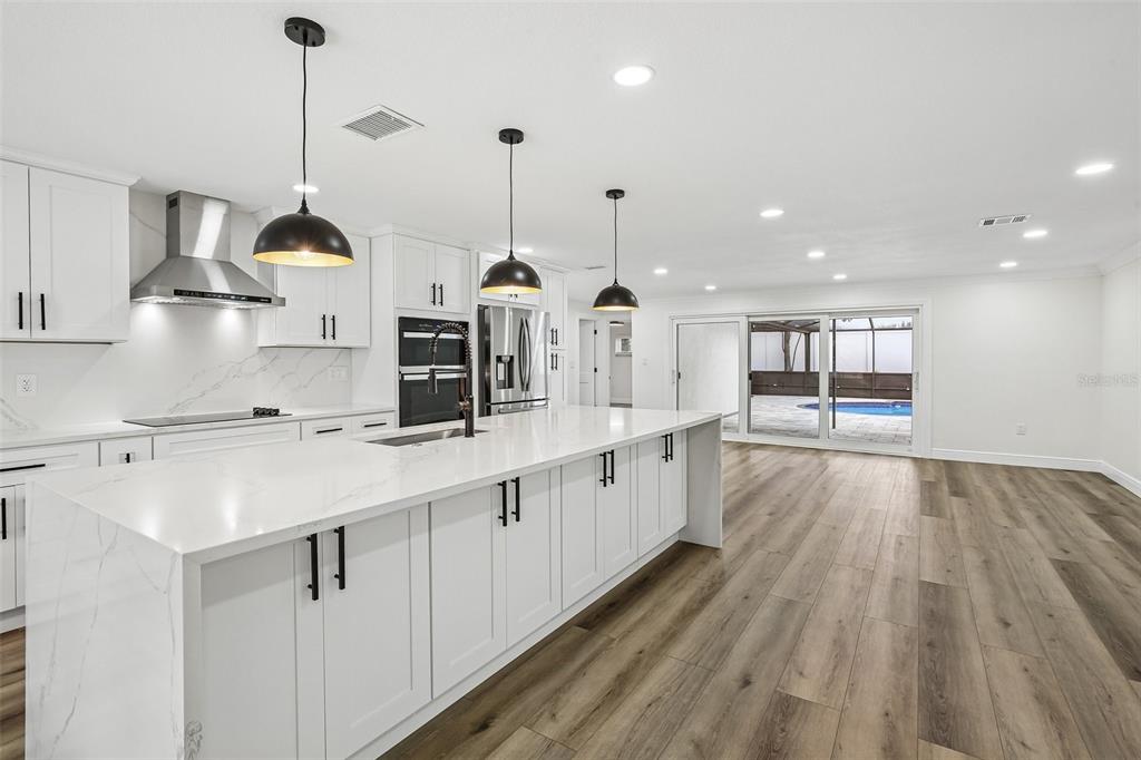 A modern white kitchen with a large island, stainless appliances, and wood-look flooring — 2230 ALBRIGHT DRIVE, CLEARWATER, FL
