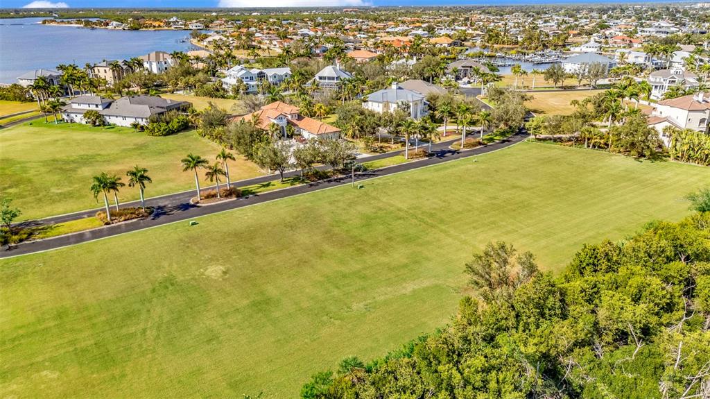 An aerial view shows a large, grassy vacant lot bordering a paved road and trees — 4661 GRASSY POINT BOULEVARD, PORT CHARLOTTE, FL