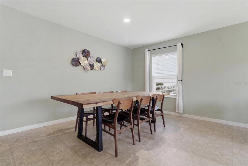 An open-concept living and dining area features a white sofa, wooden dining table, and kitchen — 10624 MASSIMO DRIVE, WIMAUMA, FL