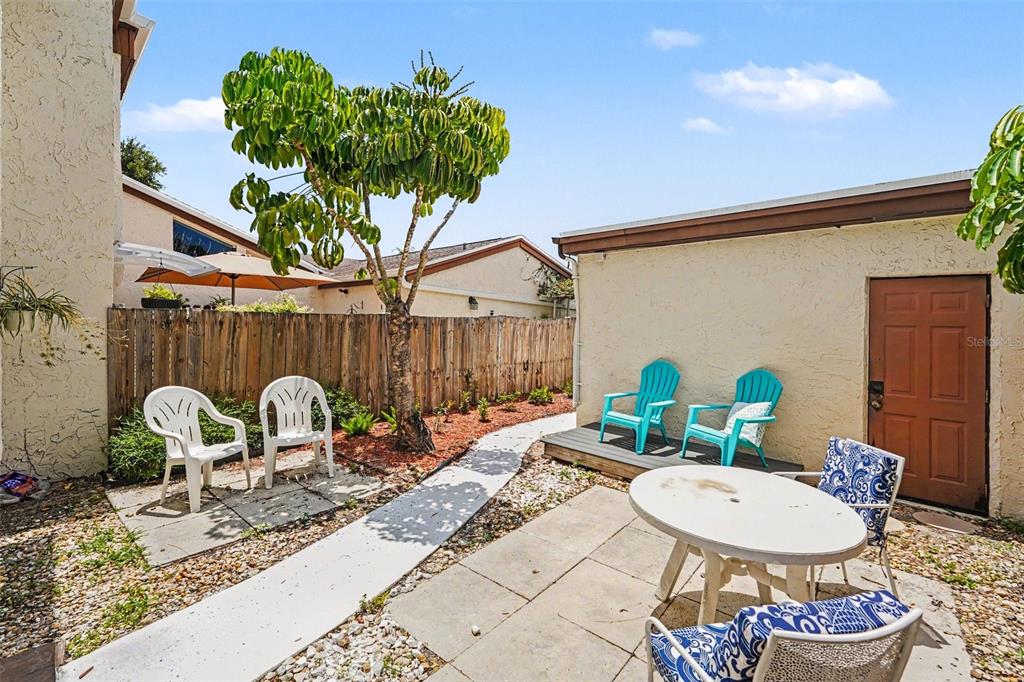 A patio area features a paved walkway, a tree, and outdoor furniture against a house — 2095 SUNSET POINT ROAD UNIT 1904, CLEARWATER, FL
