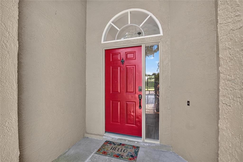 A bright red front door with a sidelight and arched transom window sits under a porch — 1434 HATCHER LOOP DRIVE, BRANDON, FL