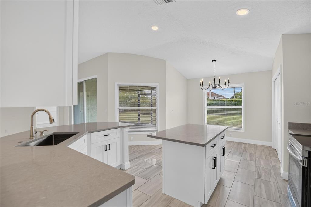 A kitchen with white cabinets, a center island, quartz countertops, and light-colored tile flooring — 1434 HATCHER LOOP DRIVE, BRANDON, FL