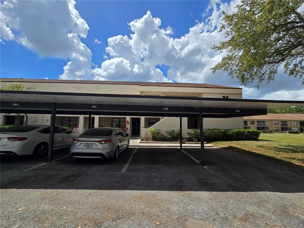 A covered parking area sits in front of a two-story apartment building under a cloudy sky — 7838 NIAGARA AVENUE UNIT 305, TAMPA, FL