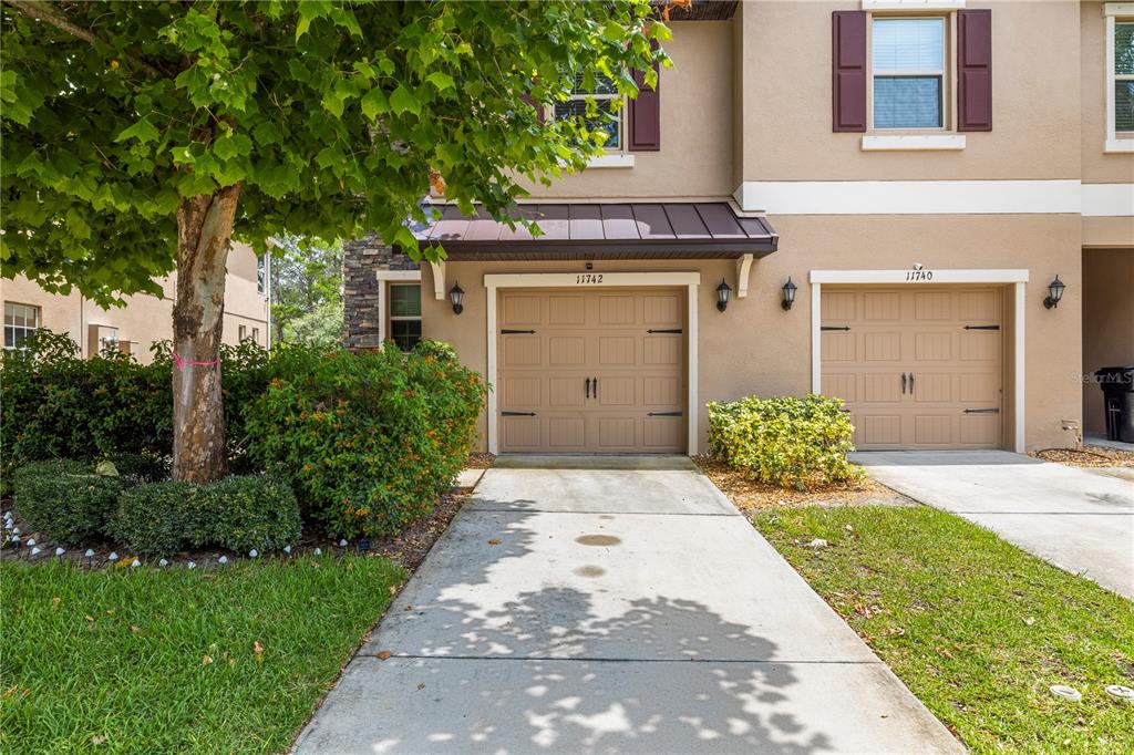 The exterior of two adjacent townhomes features tan stucco walls, brown garage doors, and landscaping — 11742 CASTINE STREET, NEW PORT RICHEY, FL