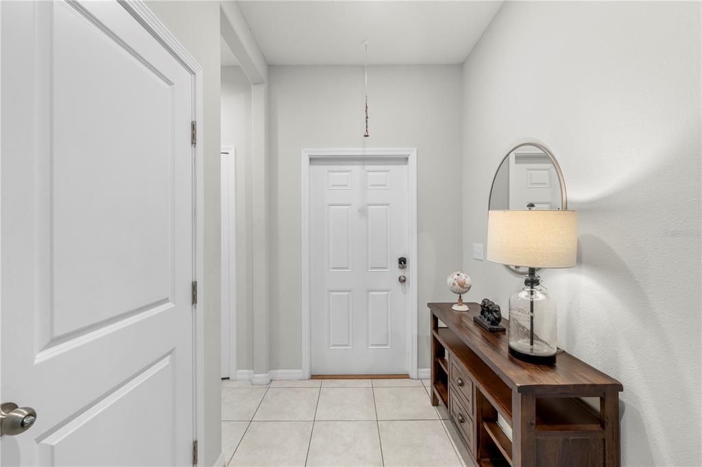 A bright entryway features white walls, tiled flooring, a wooden console table, and a front door — 11742 CASTINE STREET, NEW PORT RICHEY, FL