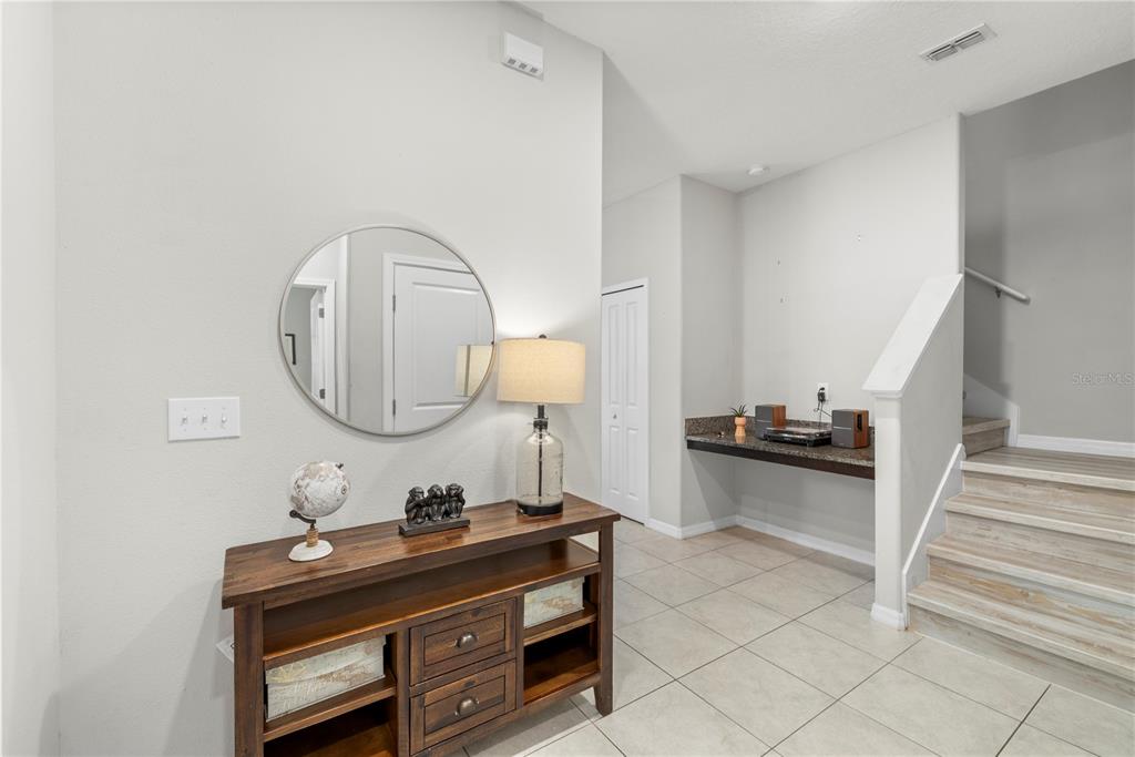 An entryway features a wooden console table, a round mirror, and stairs leading to a landing — 11742 CASTINE STREET, NEW PORT RICHEY, FL