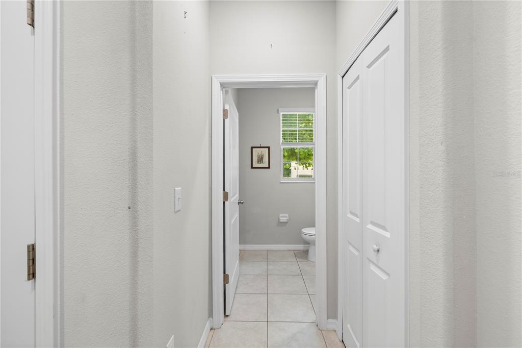 A hallway with white walls and tile flooring leads to a bathroom with a window — 11742 CASTINE STREET, NEW PORT RICHEY, FL