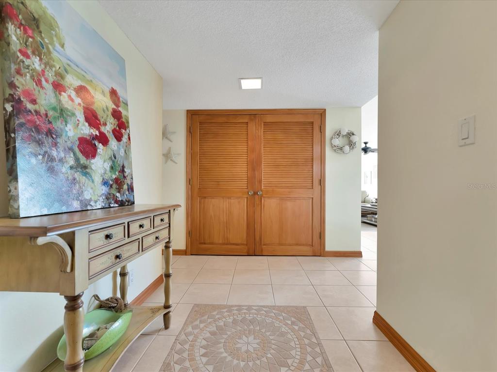A tiled entryway features a wooden console table, a floral painting, and double louvered doors — 1400 GULF BOULEVARD UNIT 204, CLEARWATER BEACH, FL
