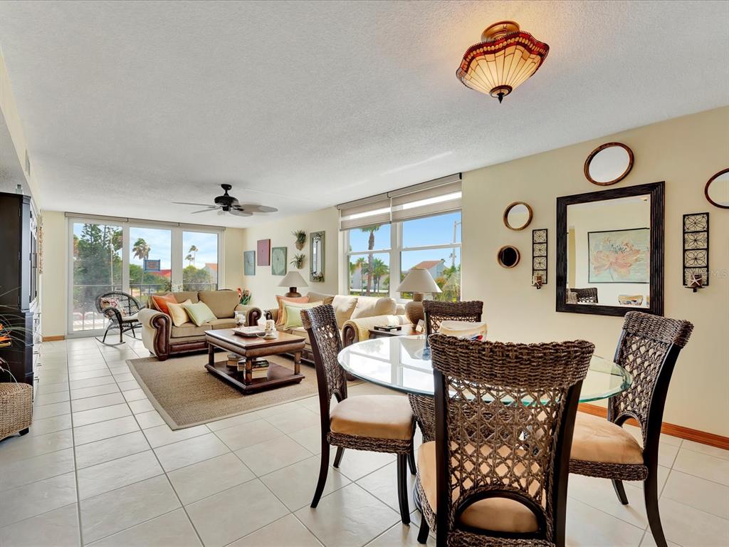 A living and dining area with tile floors, wicker furniture, and large windows overlooking palm trees — 1400 GULF BOULEVARD UNIT 204, CLEARWATER BEACH, FL