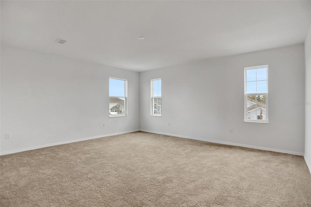 An empty room with beige carpet, light gray walls, and three windows — 7414 SEA MANATEE STREET, PARRISH, FL