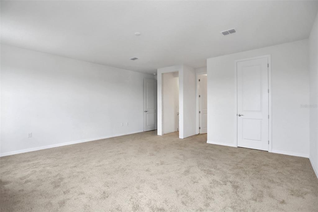 An empty bedroom with beige carpeting, white walls, and three closed interior doors — 7414 SEA MANATEE STREET, PARRISH, FL