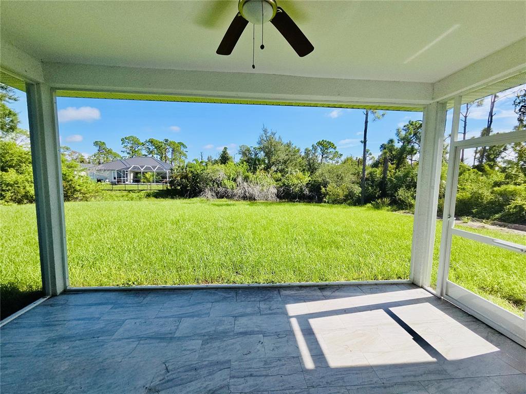 A tiled screened-in porch overlooks a grassy backyard with trees and a neighboring house — 14108 CHESSWOOD LANE, PORT CHARLOTTE, FL