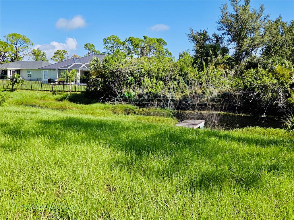 A grassy backyard features a small wooden dock extending into a pond near neighboring houses — 14108 CHESSWOOD LANE, PORT CHARLOTTE, FL