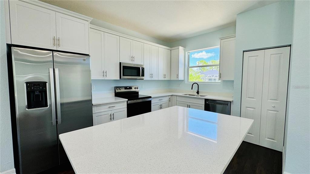 A kitchen features white cabinets, stainless steel appliances, a large island, and quartz countertops — 14108 CHESSWOOD LANE, PORT CHARLOTTE, FL