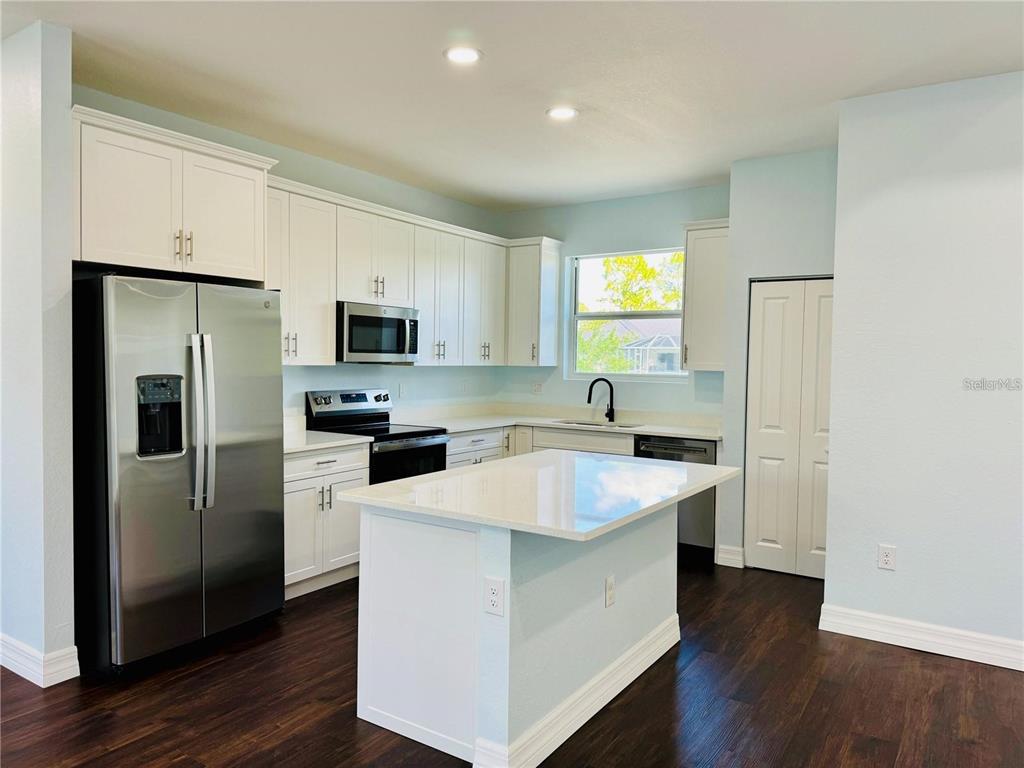 A kitchen features white cabinets, stainless steel appliances, a center island, and dark wood flooring — 14108 CHESSWOOD LANE, PORT CHARLOTTE, FL