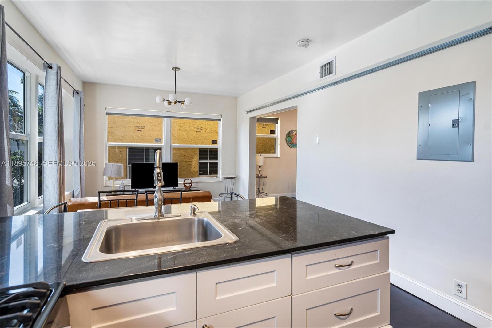 A kitchen island with a stainless steel sink sits before a living area and doorway — 1320 Drexel Ave # 200, Miami Beach FL 33139, MIAMI BEACH, FL