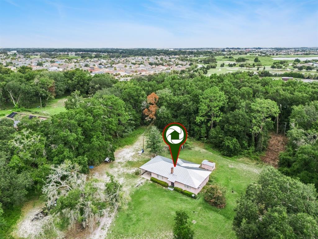 An aerial view shows a single-story house with a metal roof surrounded by wooded land — 6184 NE 54TH BOULEVARD, WILDWOOD, FL