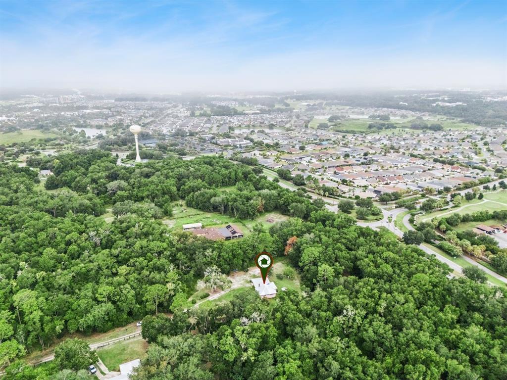 An aerial view shows a house surrounded by dense trees near a suburban residential neighborhood — 6184 NE 54TH BOULEVARD, WILDWOOD, FL