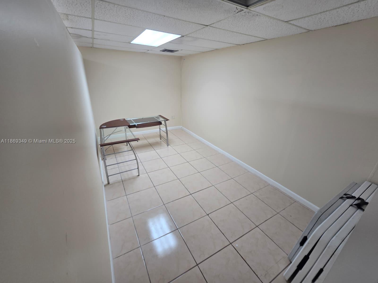 An empty office room features beige walls, a tiled floor, and a glass desk — 2501 N State Road 7 # 208, Margate FL 33063, MARGATE, FL