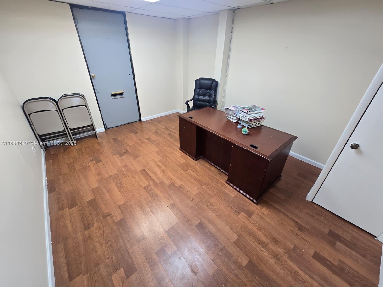 An office room features wood-look flooring, a dark wooden desk, a black chair, and two chairs — 2501 N State Road 7 # 208, Margate FL 33063, MARGATE, FL