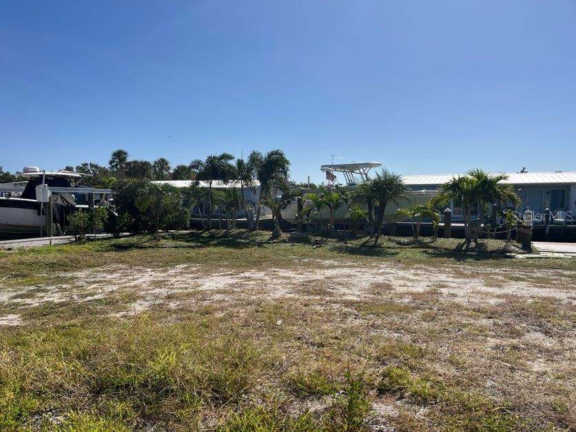 A vacant, sandy waterfront lot features palm trees and docked boats in the background — 766 SAINT JUDES DRIVE N, LONGBOAT KEY, FL