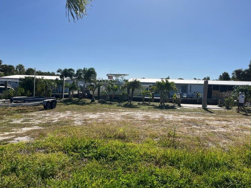 A grassy lot leads to a waterfront property with a boat dock and palm trees — 766 SAINT JUDES DRIVE N, LONGBOAT KEY, FL