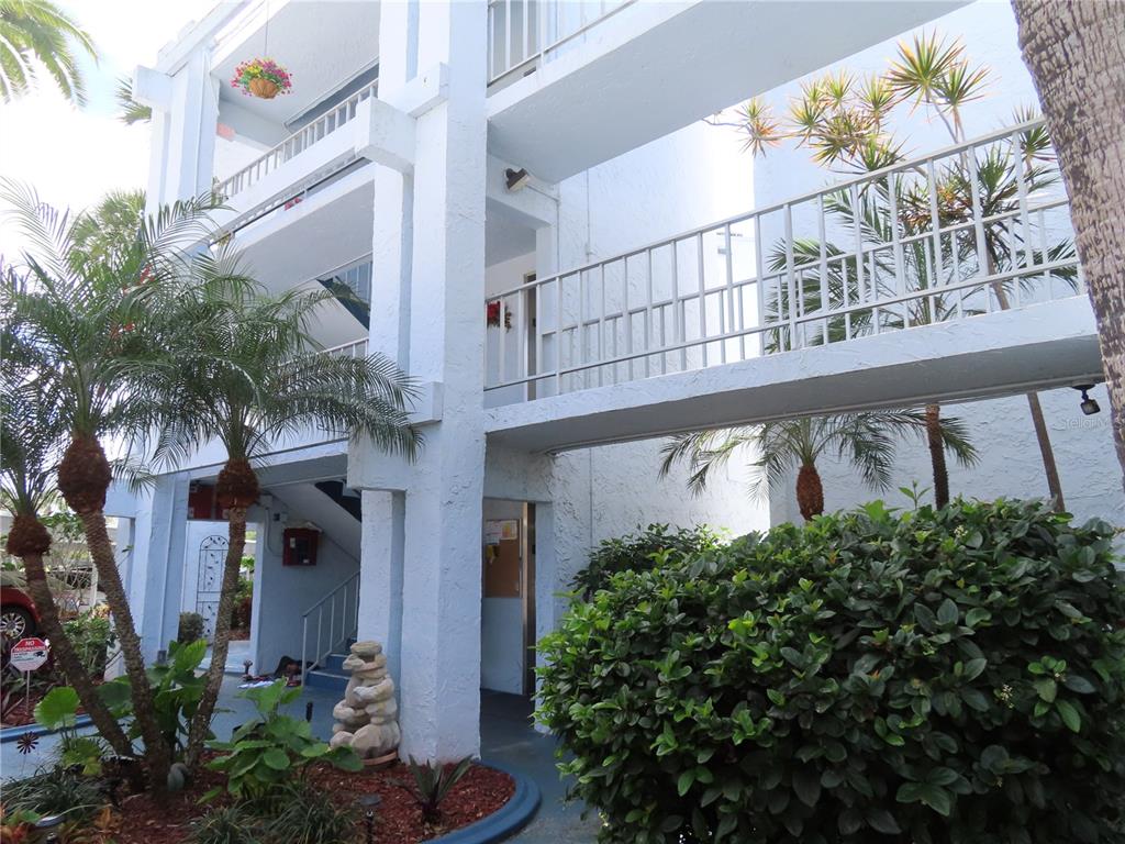 A multi-story white building features open-air walkways, palm trees, and a landscaped garden area — 225 COUNTRY CLUB DRIVE UNIT C225, LARGO, FL