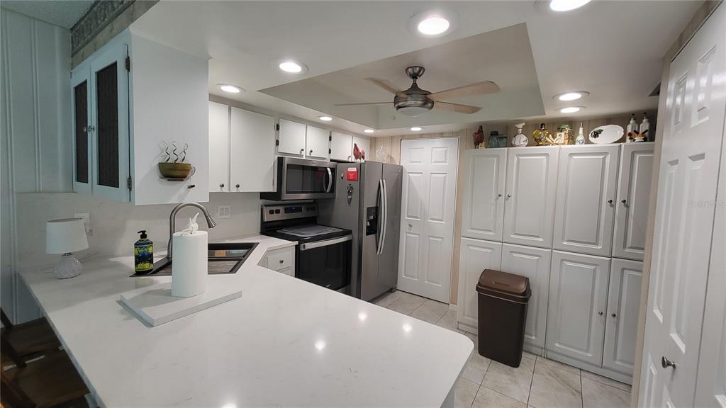 A kitchen features white cabinets, quartz countertops, stainless steel appliances, and a ceiling fan — 225 COUNTRY CLUB DRIVE UNIT C225, LARGO, FL