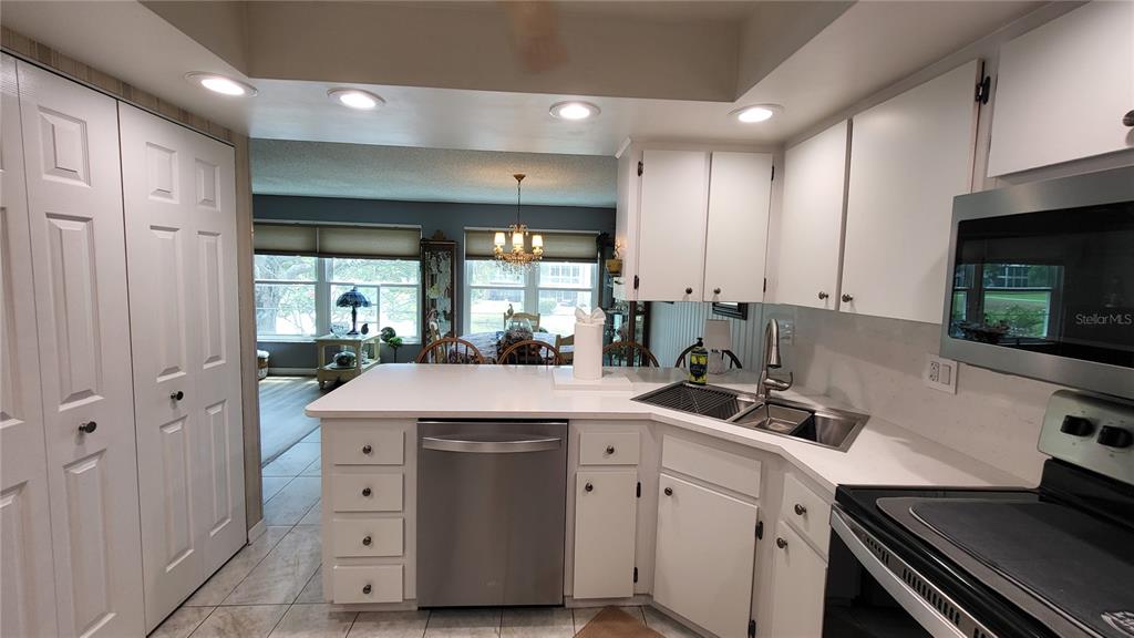 A kitchen with white cabinets, stainless steel appliances, and a peninsula overlooking a dining area — 225 COUNTRY CLUB DRIVE UNIT C225, LARGO, FL