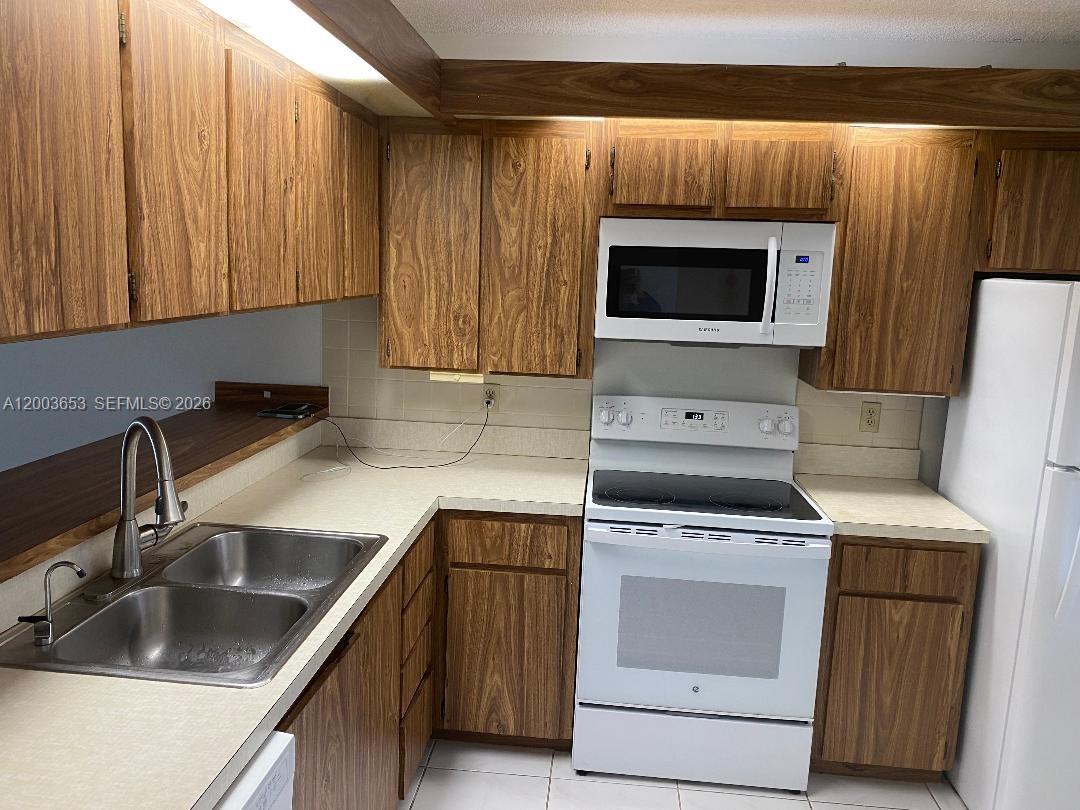 A kitchen features wood-grain cabinets, white appliances, a double sink, and laminate countertops — 1701 Whitehall Dr # 403, Davie FL 33324, DAVIE, FL