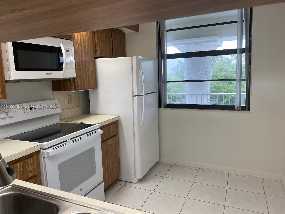 A kitchen features white appliances, wood cabinets, tiled floors, and a window with balcony views — 1701 Whitehall Dr # 403, Davie FL 33324, DAVIE, FL