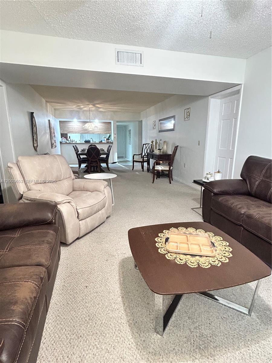 A living room with carpeted floors, brown leather furniture, and a dining area in back — 1701 Whitehall Dr # 403, Davie FL 33324, DAVIE, FL