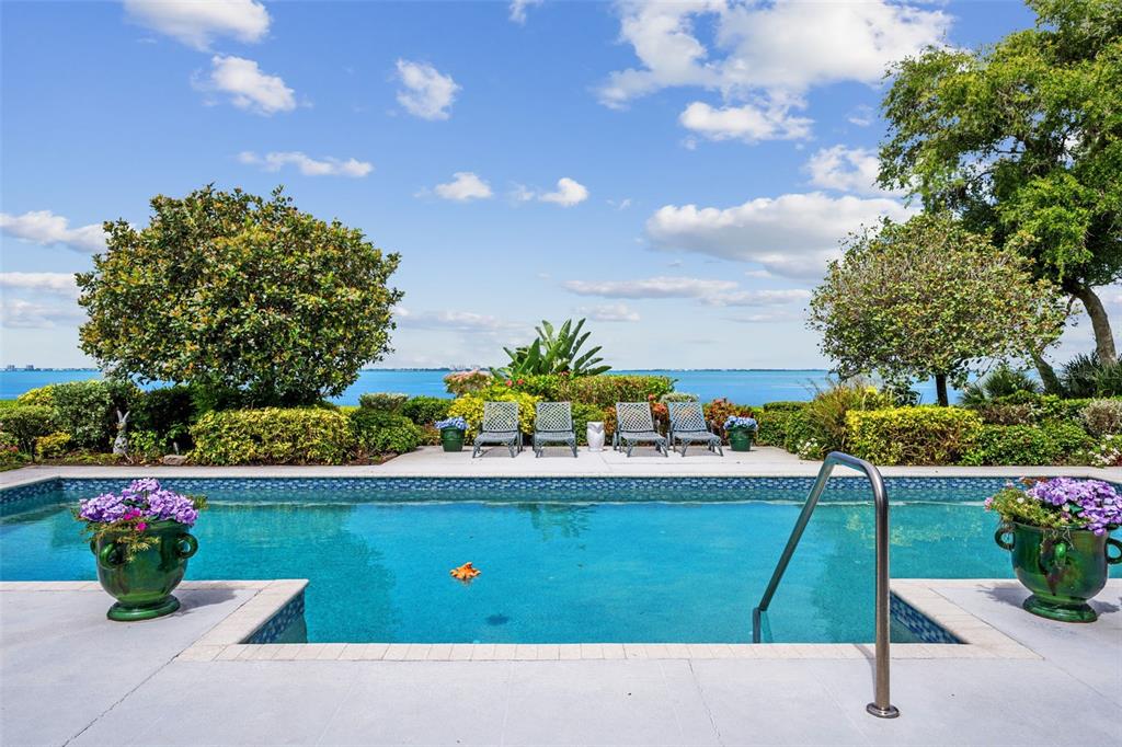 A swimming pool with lounge chairs overlooks a large body of water under a blue sky — 8152 LONGBAY BOULEVARD, SARASOTA, FL