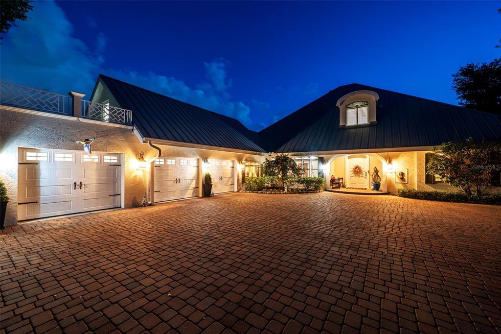 A paved driveway leads to a house with a three-car garage and metal roof — 8152 LONGBAY BOULEVARD, SARASOTA, FL