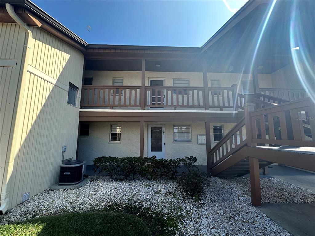 A two-story apartment building exterior features a wooden staircase, balcony, and gravel landscaping — 5154 TURQUOISE LANE UNIT 206, NEW PORT RICHEY, FL