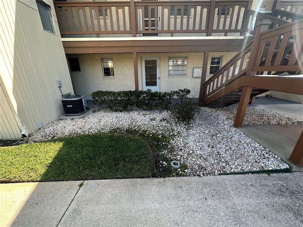Exterior view of a ground-floor apartment entrance with a wooden staircase and gravel landscaping — 5154 TURQUOISE LANE UNIT 206, NEW PORT RICHEY, FL