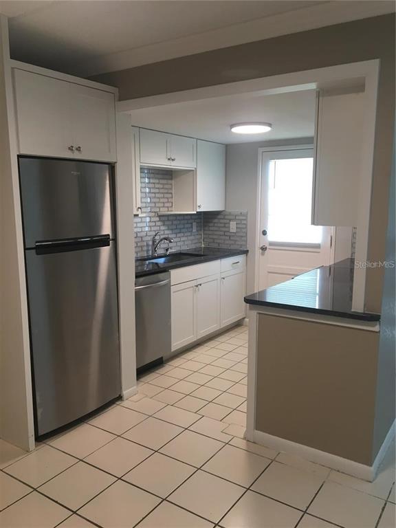 A kitchen features white cabinets, stainless steel appliances, a tiled backsplash, and a breakfast bar — 2 N FERNWOOD AVENUE UNIT 7, CLEARWATER, FL