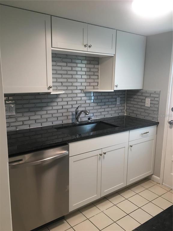 A kitchen features white cabinets, a black countertop, a stainless steel dishwasher, and gray backsplash — 2 N FERNWOOD AVENUE UNIT 7, CLEARWATER, FL